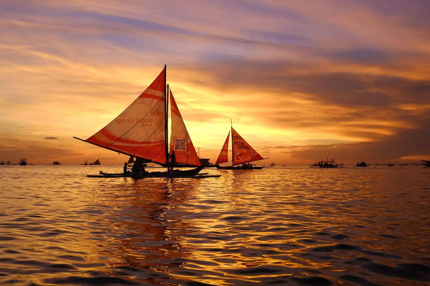 Traditional paraw sailboats gliding across the water at sunset in Boracay