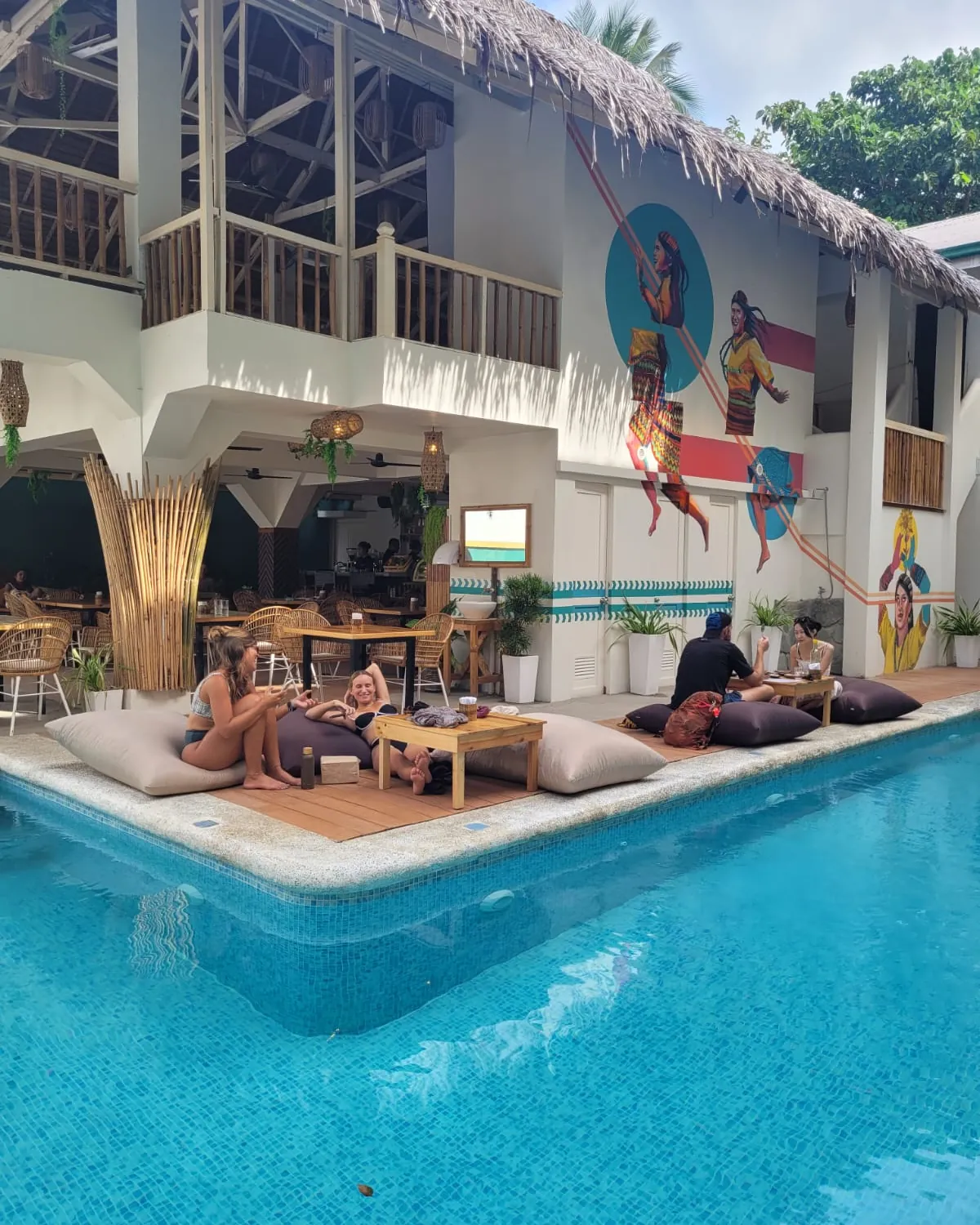 Guests lounging on bean bags beside the hostel pool under murals