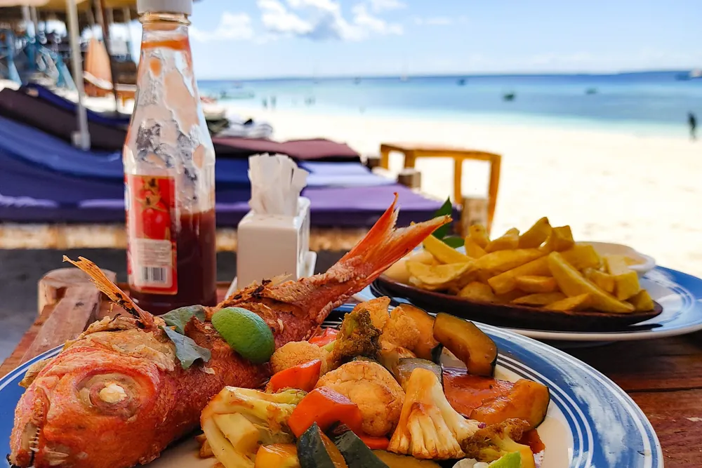 Grilled fish and seafood platter with a cold drink at a beach table under a parasol