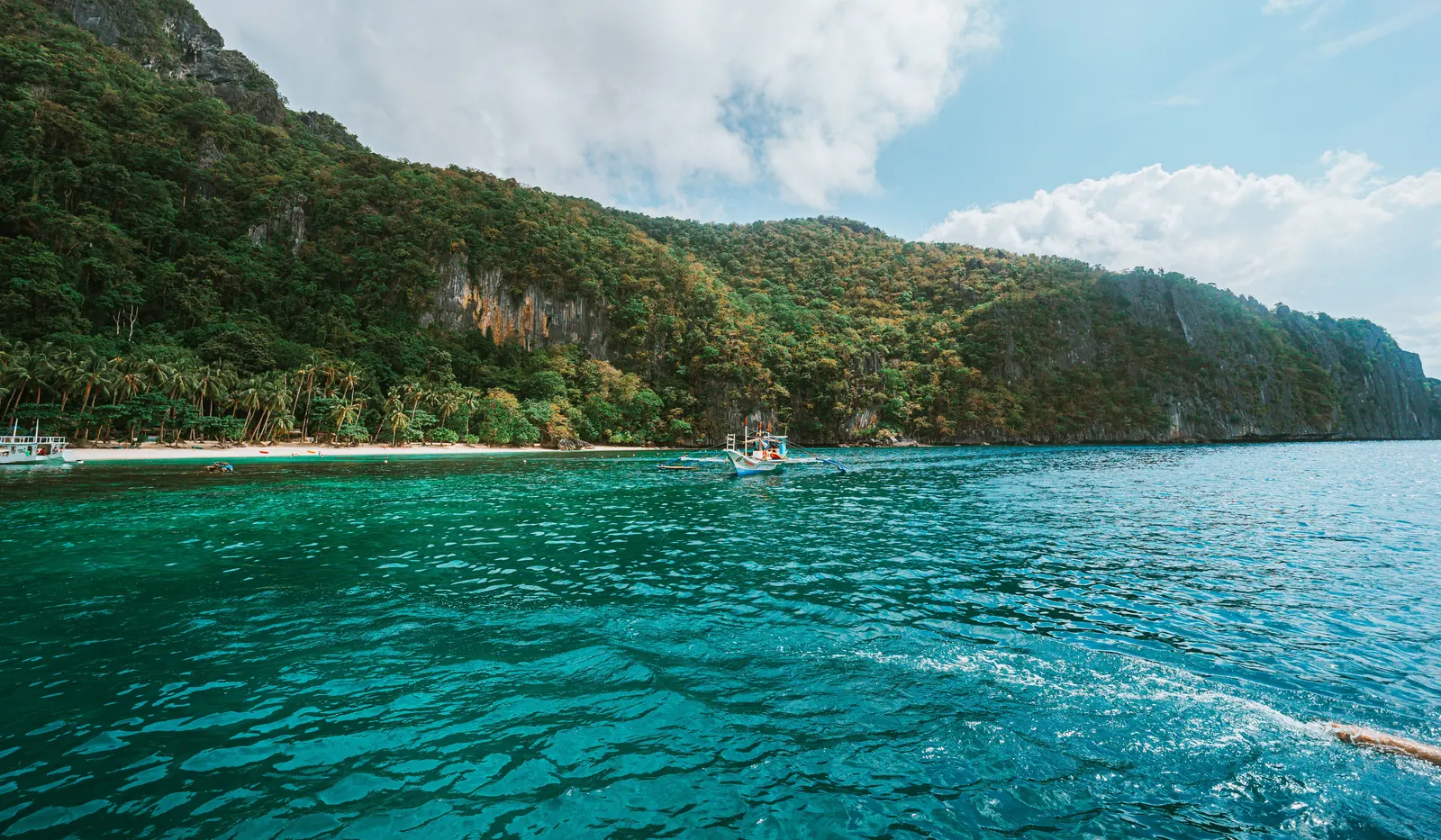 Turquoise water and a green limestone island in El Nido on a sunny day