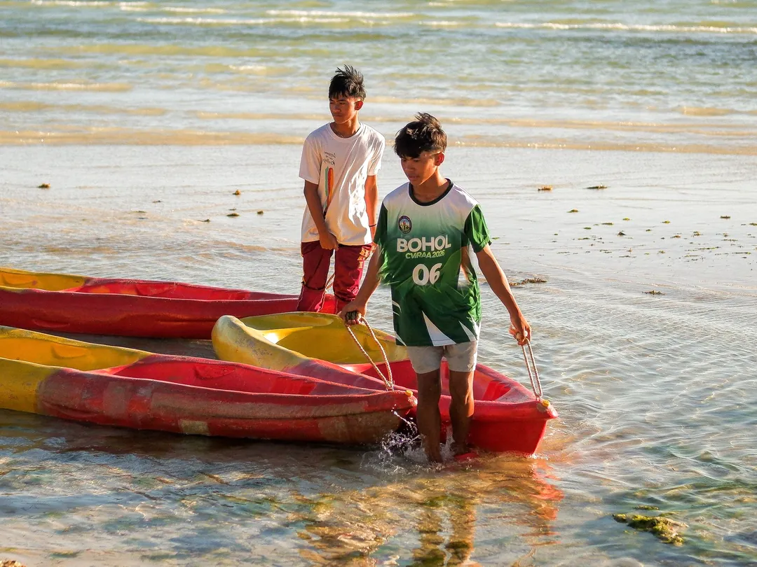 Two kids pulling kayaks into calm shallow water