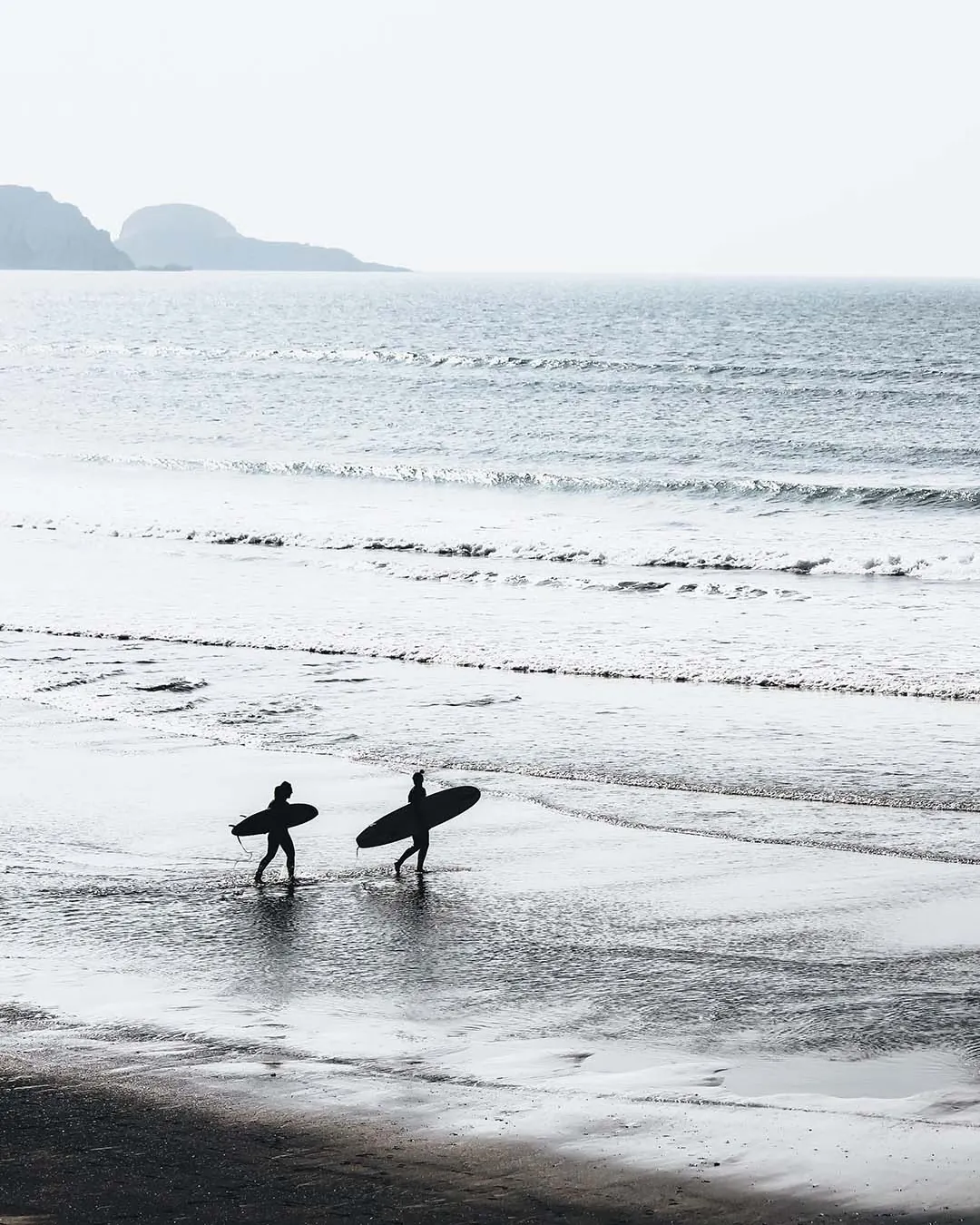Two surfers walking along the shore at dawn with boards under their arms