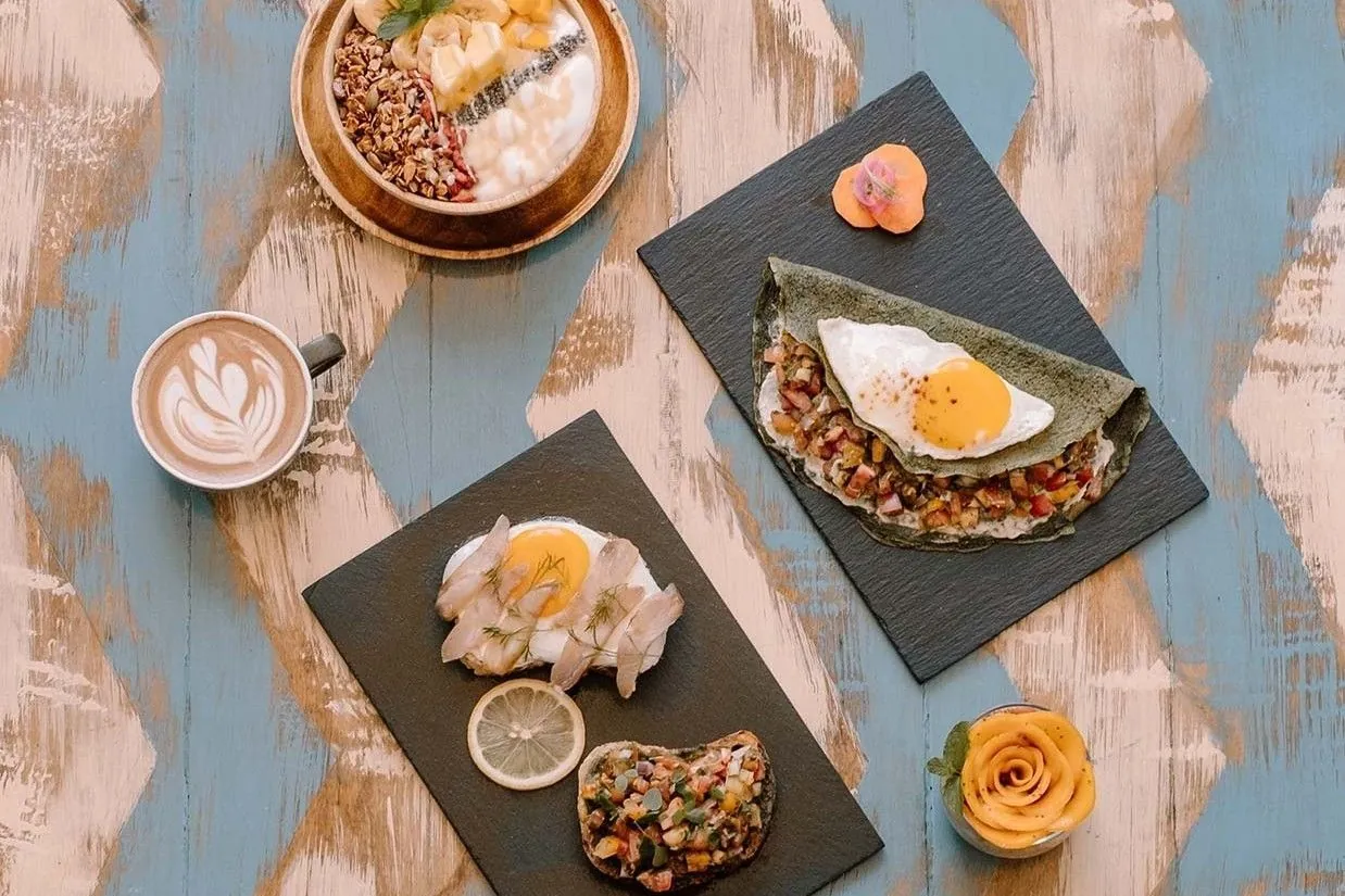 Colourful plates and coffee on a blue tiled table at Happiness Restaurant