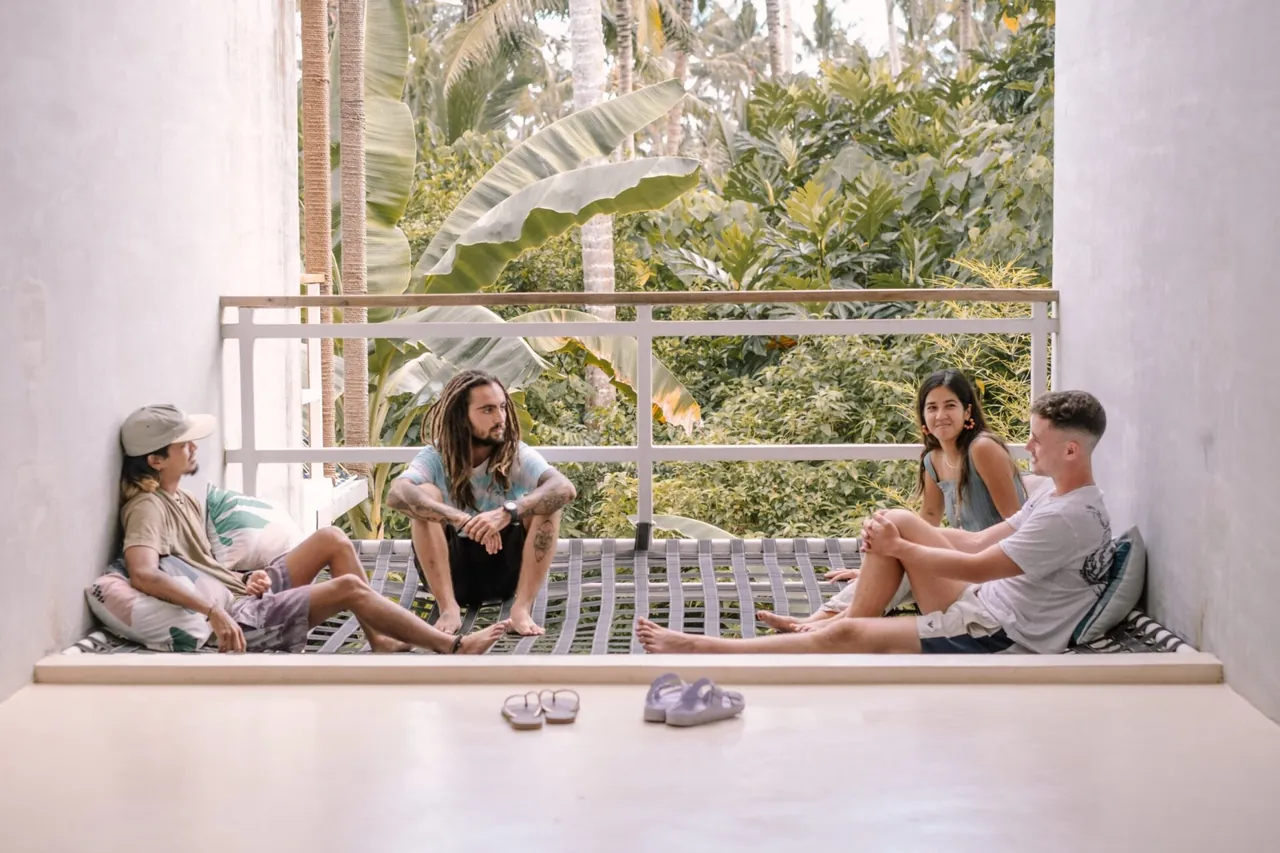 Friends chatting on a sunny hostel balcony above the palms