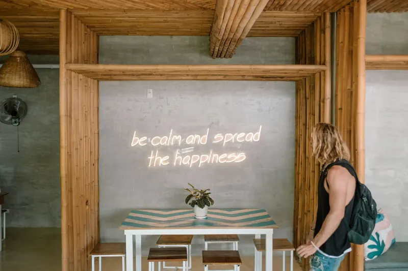 A guest at a reception desk under a neon sign reading be calm and spread the happiness