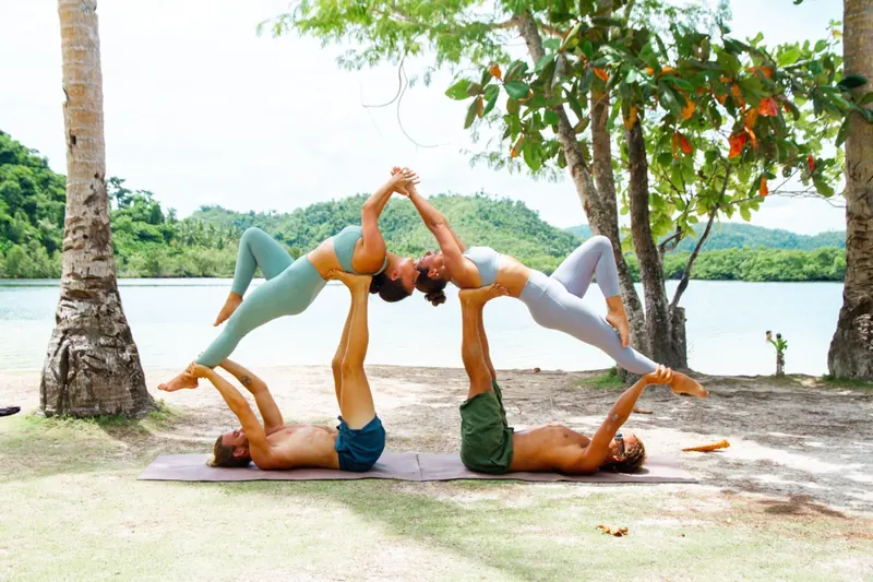 Two guests practising acro yoga on the grass by the sea