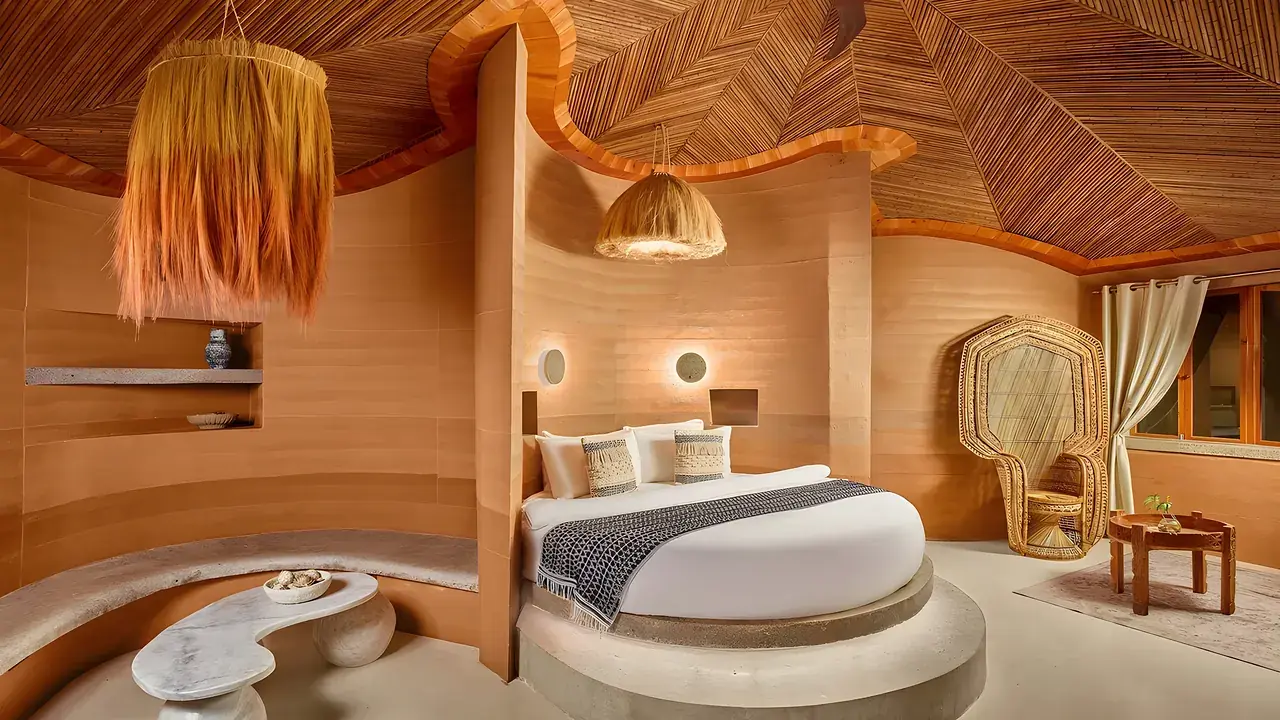 A sculpted resort room with a round bed and woven pendant lights