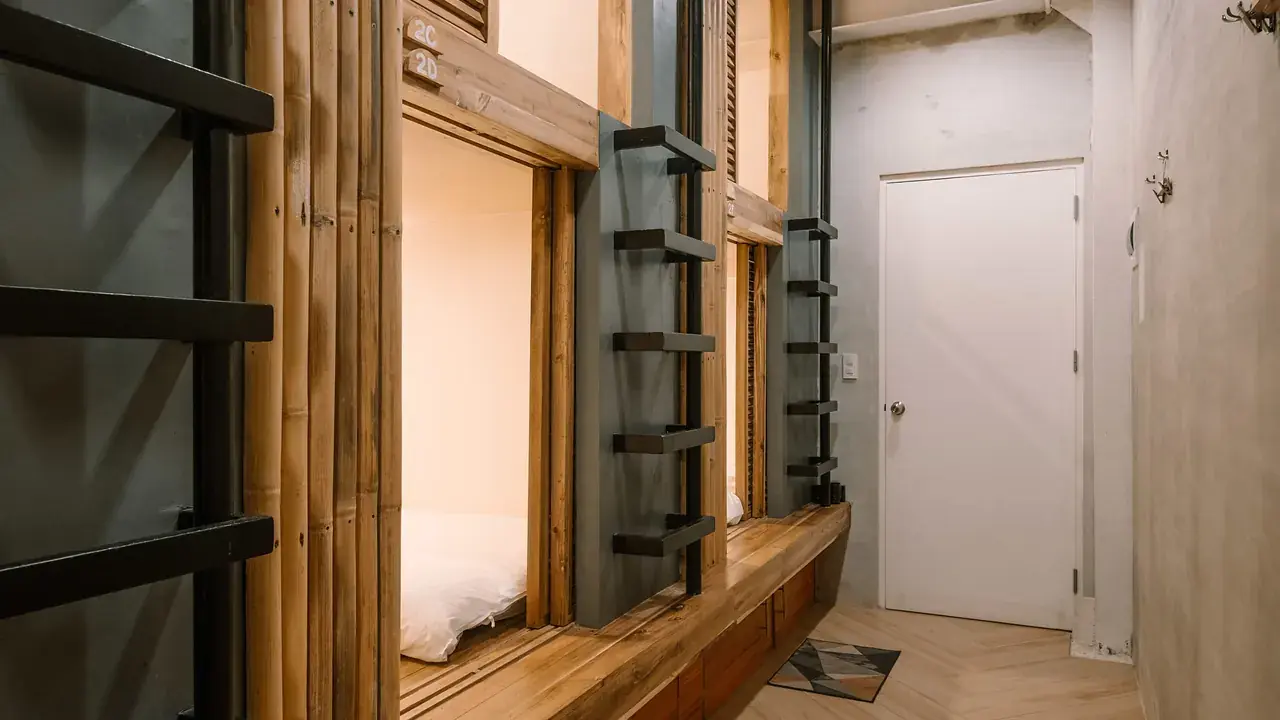 Wooden dorm pods along a bright hostel corridor