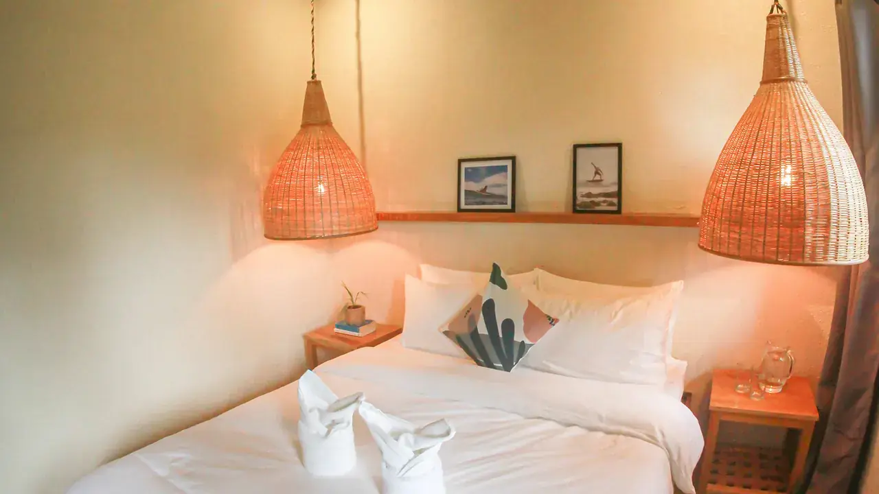 A private room with woven lamps and a white double bed