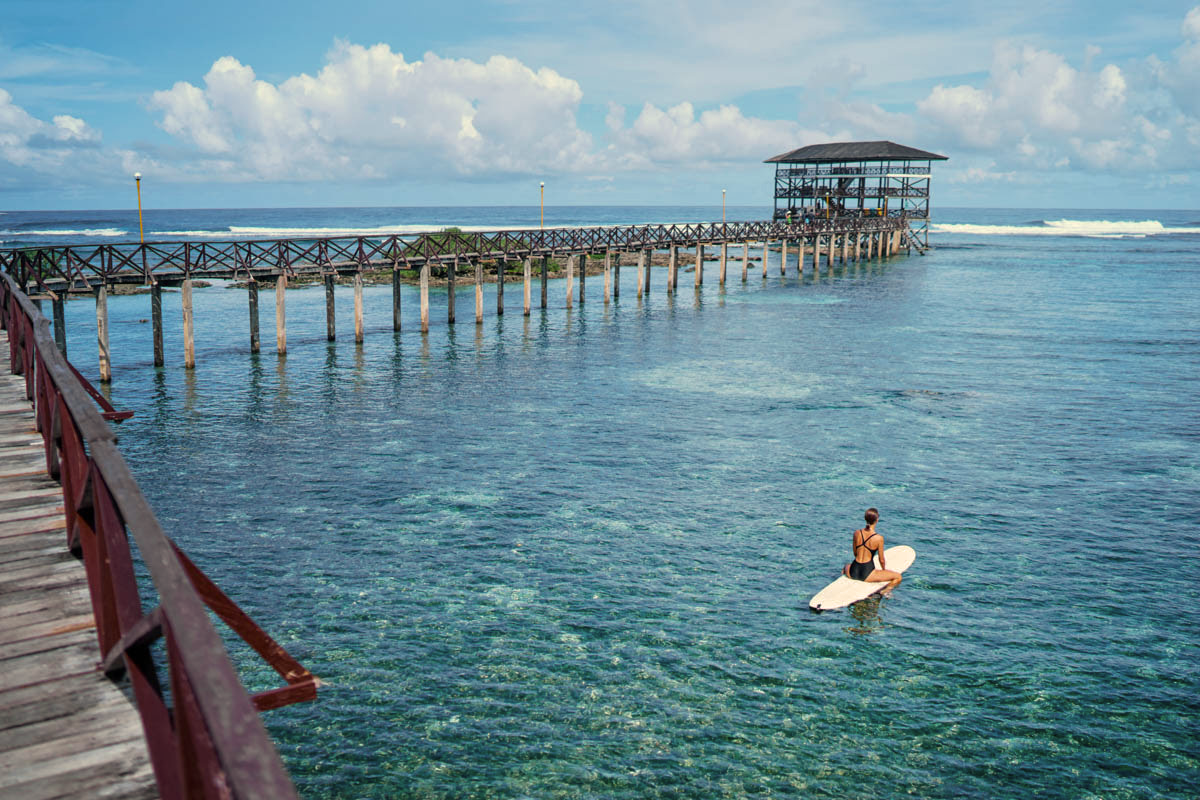 Surfer paddling past the Cloud 9 boardwalk in Siargao